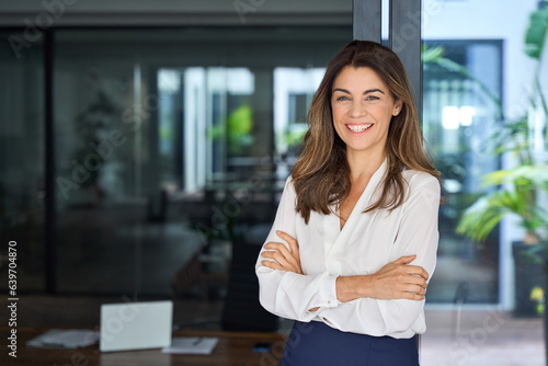 Happy cheerful 45 year old Latin professional mid aged business woman corporate leader, smiling positive mature female executive manager standing in office arms crossed looking at camera, portrait. photo