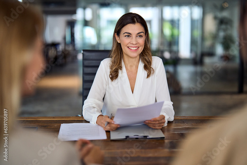 Smiling mature middle aged professional business woman banking loan manager, insurance agent, lawyer or financial advisor consulting clients couple sitting at work corporate office meeting.