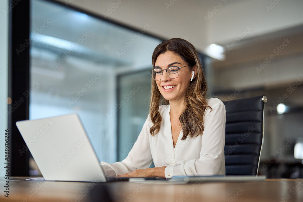 Happy mid aged business woman having hybrid meeting working in office. Busy mature female corporate leader executive, hr manager communicating by conference call, remote online job interview on laptop Happy mid aged business woman having hybrid meeting working in office. Busy mature female corporate leader executive, hr manager communicating by conference call, remote online job interview on laptop