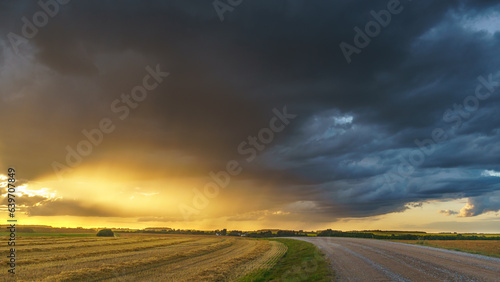 A black rain cloud over a rural field. The rays of the setting sun are breaking through a terrible gray cloud. On the eve of the storm. Bad weather conditions.