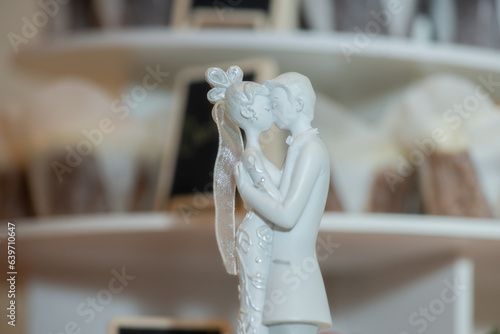 Bride and groom passionately kissing ceramic cake toppers on top of cake and infromt of out of focus cup cakes mid photo