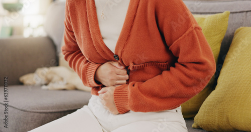 Stomach ache, cramps and hands of woman with abdomen pain due to constipation, menstruation or ibs issue. Sick, home and person suffering and holding belly in a house lounge, couch and living room photo