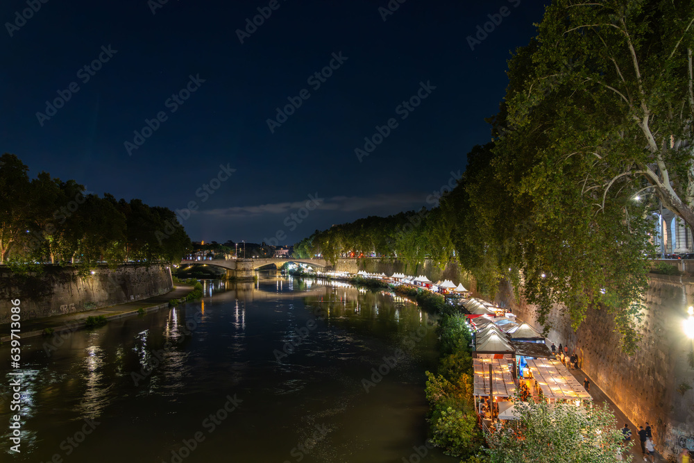 Vatican City in the distance with the Tiber river and pop-up restaurants on its banks, in Rome, Italy, at night Vatican City in the distance with the Tiber river and pop-up restaurants on its banks, in Rome, Italy, at night