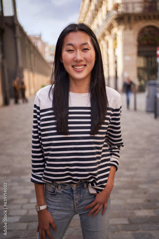 Vertical portrait of happy beautiful young Asian woman happy smiling face on street. Female people with cheerful expression looking at camera in open air. Chinese girl posing hand in pocket outdoor. Vertical portrait of happy beautiful young Asian woman happy smiling face on street. Female people with cheerful expression looking at camera in open air. Chinese girl posing hand in pocket outdoor.