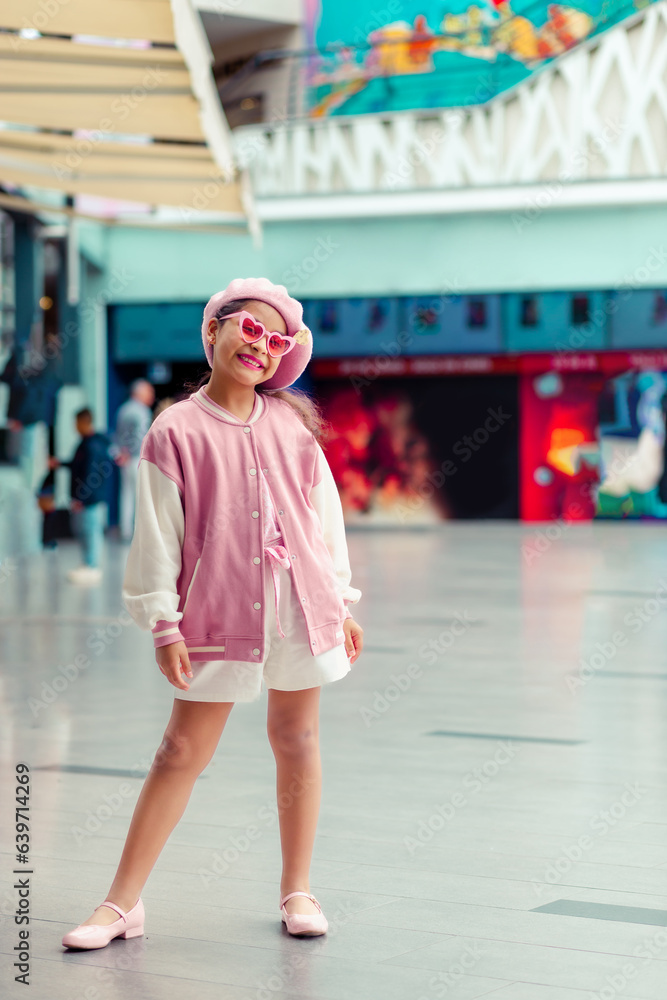 Retrato de linda niña sonriente con atuendo rosa y gafas  de sol rosa en el centro comercial.