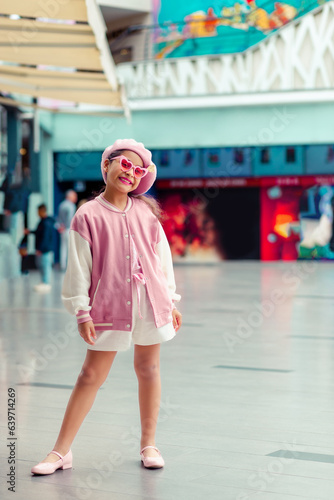 Retrato de linda niña sonriente con atuendo rosa y gafas de sol rosa en el centro comercial.