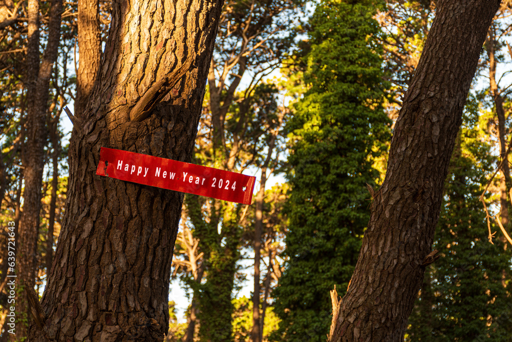 Red sheet metal sign with Happy New Year 2024 text in white on a tree.
