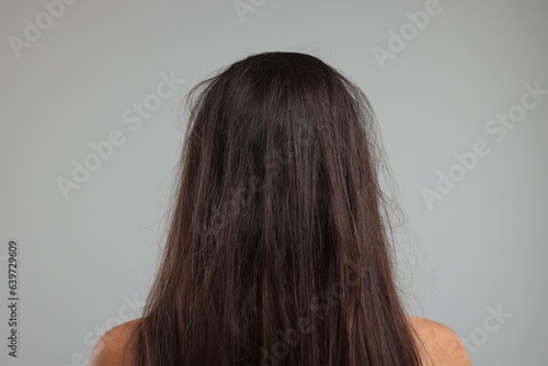 Woman with damaged messy hair on grey background, back view