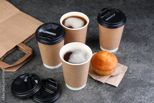 Coffee to go. Paper cups with tasty drink and muffin on grey table