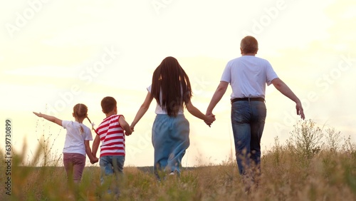 Family with little children plays plane and runs across meadow grass at sunset