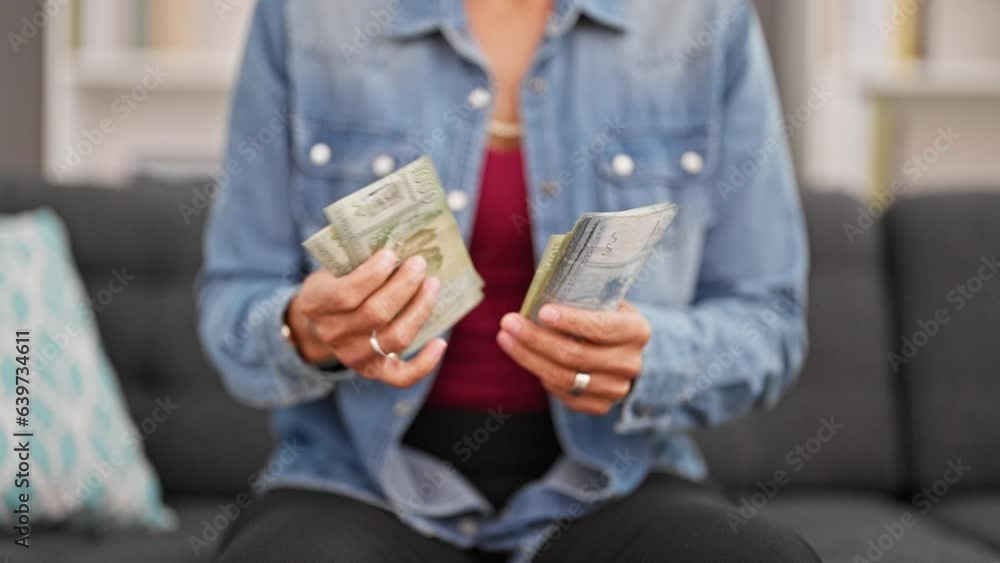 Young beautiful hispanic woman counting chilean pesos banknotes at home
