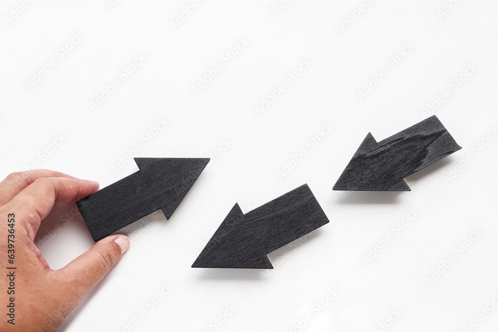 Obraz premium Finger pushing wooden arrows point up. close up of hand picked up wooden arrows point and two arrows point down on white background. Business concept.