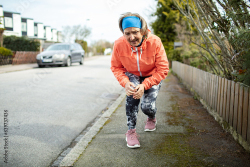 Senior caucasian woman getting her knee joint injured while jogging and exercising in the suburbs photo