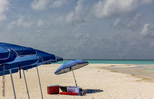 Beach umbrellas stand together for tourists at a clean and quiet sandy beach with blue sky background.