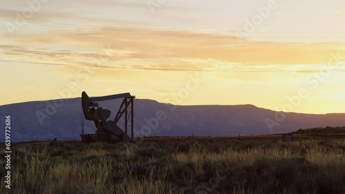 Oil pump works in large desert field as sun rises over beautiful Utah mountains