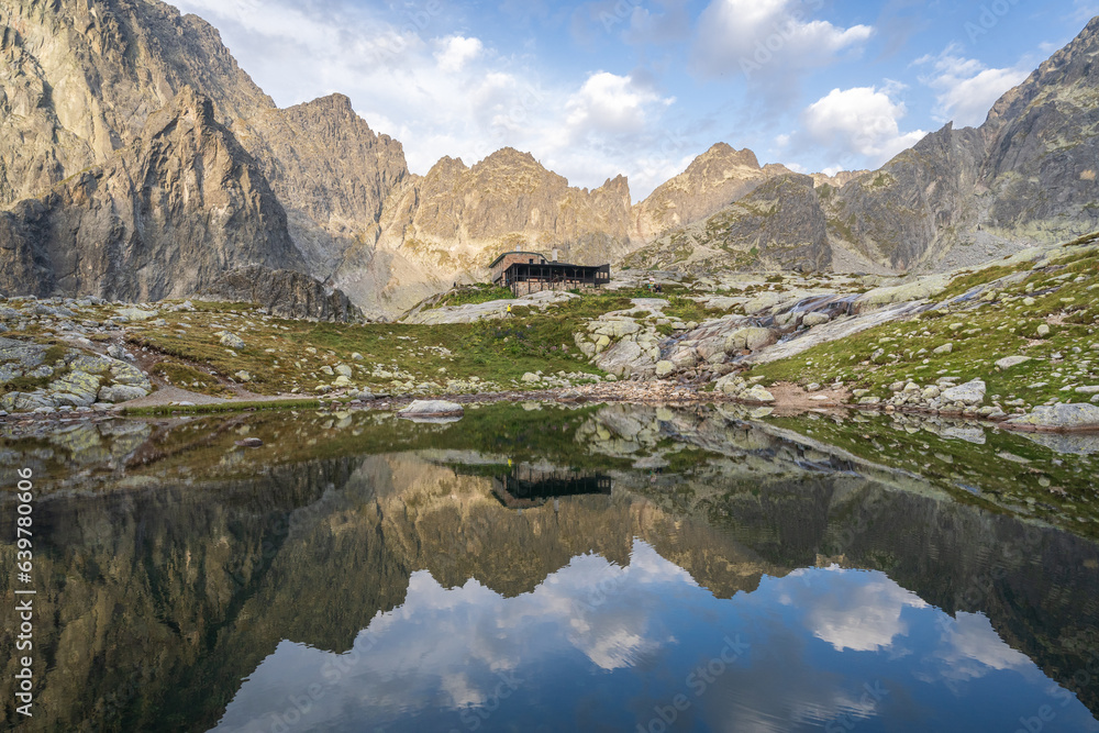 Alpine hut surrounded by mountains reflected in foreground tarn during sunrise, Slovakia, Europe