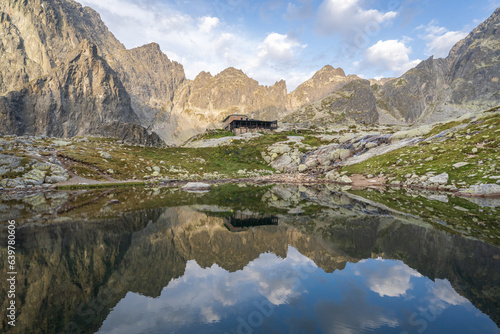 Alpine hut surrounded by mountains reflected in foreground tarn during sunrise, Slovakia, Europe