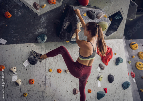 A strong female climber climbs an artificial wall with colorful grips and ropes.