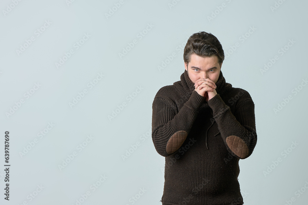 a man in a gray sweater on a gray background shows that he is cold a man in a gray sweater on a gray background shows that he is cold
