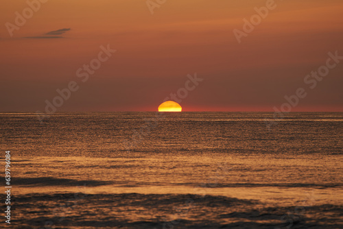 The glowing sun sinking on the horizon of the sea or ocean