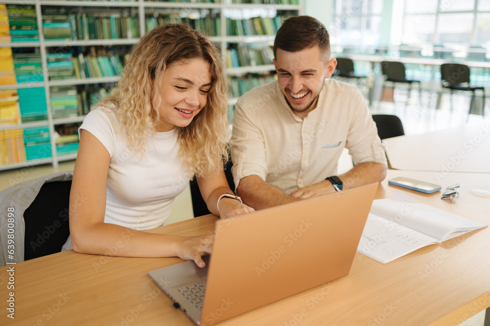 Two classmate look into laptop and laugh. Boy and girl study in library. University concept Two classmate look into laptop and laugh. Boy and girl study in library. University concept