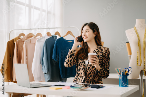 Asian tailor woman working on clothes in tailoring atelier. beautiful young female fashion designer smile and after success in modern tudio photo