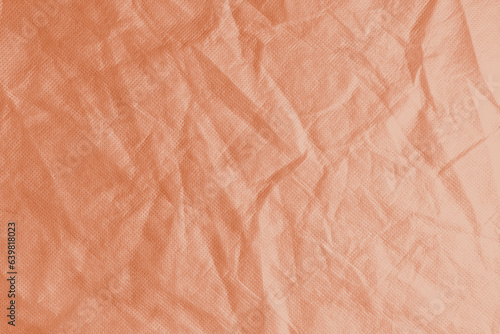 Wrinkled, crumpled orange fabric texture background. Wrinkled and creased abstract backdrop of spunbond textile, wallpaper with copy space, top view.