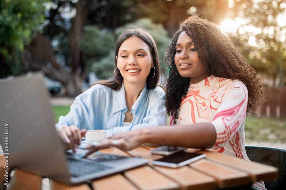 Happy Multiethnic Female Friends Using Laptop Computer Together Outdoors At Cafe Terrace Happy Multiethnic Female Friends Using Laptop Computer Together Outdoors At Cafe Terrace