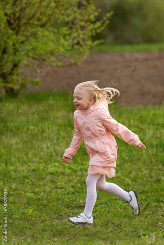 Portrait of little European girl with blonde hair in pink outfit running across field. Vertical frame. © somemeans