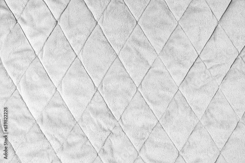 Quilted velours fabric background. White texture blanket or puffer jacket, stiched with diamond pattern, soft wrinkled surface, crupmed textile photo