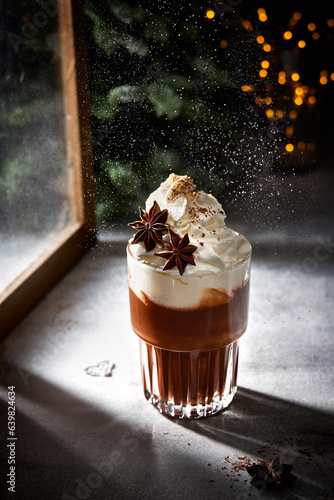 Glass of hot chocolate with whipped cream. Sugar powder snow. Christmas lights. Cozy winter still life.