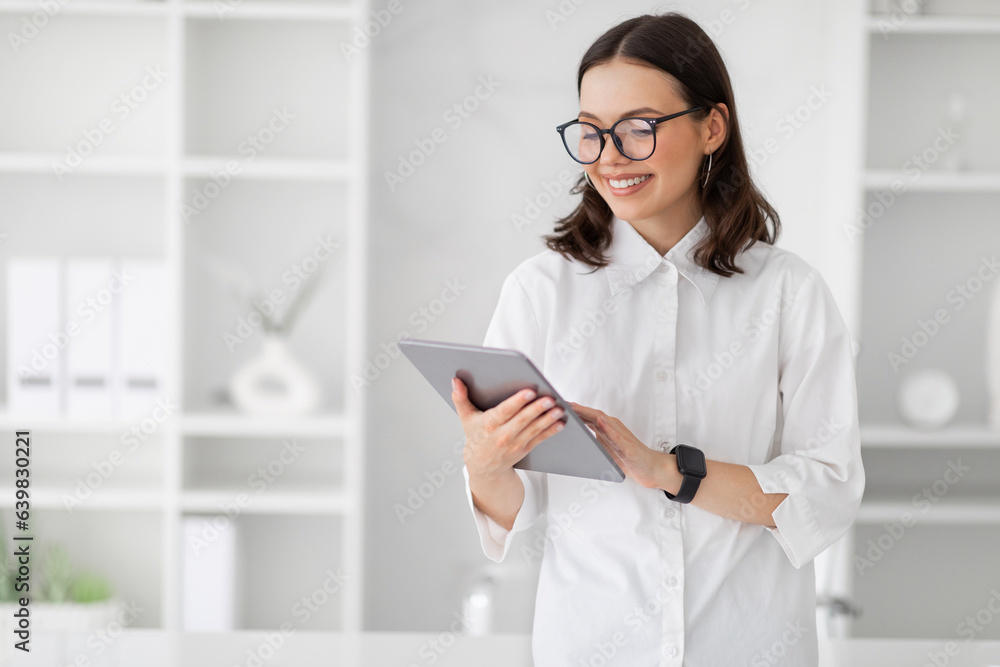 Positive millennial european business lady in glasses uses tablet to chat, enjoy work Positive millennial european business lady in glasses uses tablet to chat, enjoy work