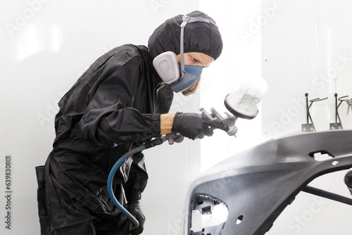Worker painting car parts with compressor, side view