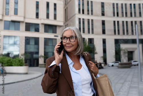 successful senior woman in a brown suit holds a call to a business partner on the street