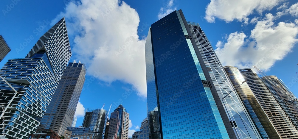 Fototapeta premium Downtown, skyscrapers in Sydney, below view. Huge buildings, highrise towers, blue cloudy sky.