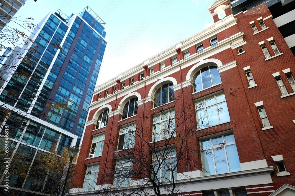 Obraz premium A reddish building with arched windows trimmed in white, a dry tree in front of the building, and a bright blue sky, Melbourne, Australia