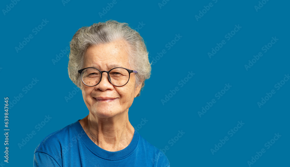 Beautiful senior woman with short white hair and glasses smiles at the camera while standing against a blue background. Beautiful senior woman with short white hair and glasses smiles at the camera while standing against a blue background.