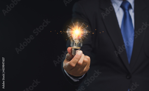 Close-up of hand a businessman holding a lighting bulb with lighting while standing on a black background