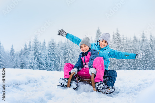 Family are sledding. Happy children run on wooden sleds down the slope. Winter sports entertainment for children. Wonderful snowy landscape background.