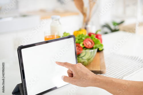 Female hands pointing tablet blank screen, searching healthy menu recipe on the internet over her dining table. Phone white screen with healthy food concept