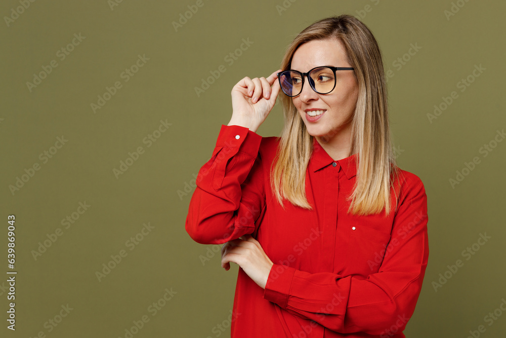 Young smiling minded fun woman she wearing red shirt casual clothes touch glasses looking aside on workspace area mock up isolated on plain pastel green background studio portrait. Lifestyle concept. Young smiling minded fun woman she wearing red shirt casual clothes touch glasses looking aside on workspace area mock up isolated on plain pastel green background studio portrait. Lifestyle concept.