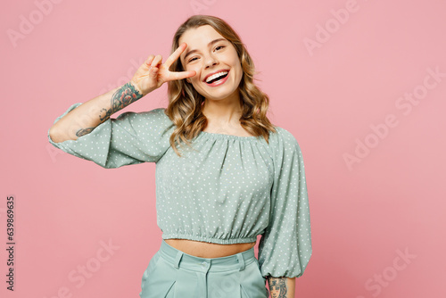 Young smiling cheerful fun happy woman she wear casual clothes look camera show cover eye with victory gesture v-sign isolated on plain pastel light pink background studio portrait. Lifestyle concept.