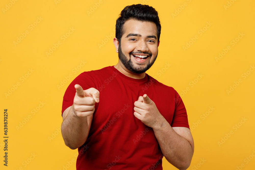 Young confident leader happy Indian man he wears red t-shirt casual clothes point index finger camera on you motivating encourage isolated on plain yellow orange background studio. Lifestyle concept. Young confident leader happy Indian man he wears red t-shirt casual clothes point index finger camera on you motivating encourage isolated on plain yellow orange background studio. Lifestyle concept.