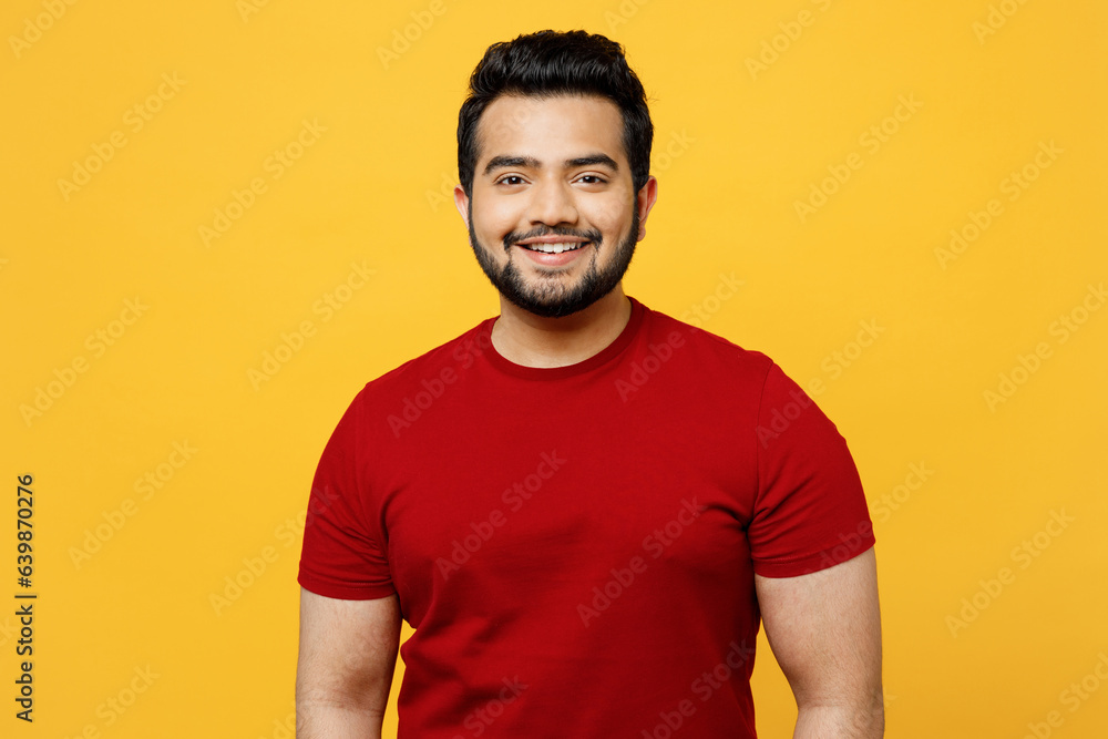 Young smiling satisfied positive cheerful optimist happy Indian man he wearing red t-shirt casual clothes looking camera isolated on plain yellow orange background studio portrait. Lifestyle concept. Young smiling satisfied positive cheerful optimist happy Indian man he wearing red t-shirt casual clothes looking camera isolated on plain yellow orange background studio portrait. Lifestyle concept.