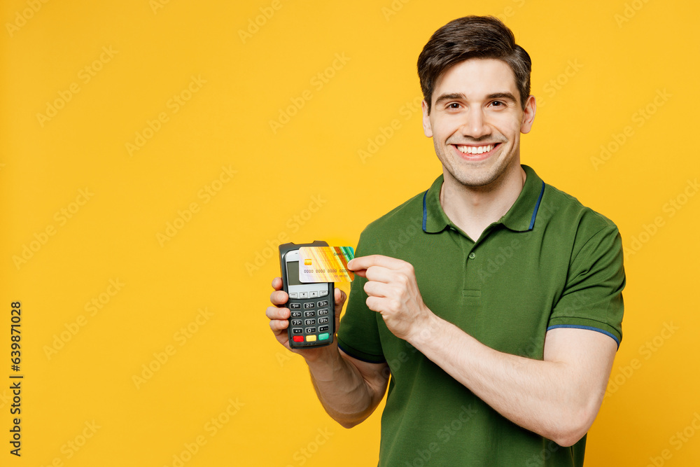 Young happy man he wears green t-shirt casual clothes hold wireless modern bank payment terminal to process acquire credit card isolated on plain yellow background studio portrait. Lifestyle concept. Young happy man he wears green t-shirt casual clothes hold wireless modern bank payment terminal to process acquire credit card isolated on plain yellow background studio portrait. Lifestyle concept.
