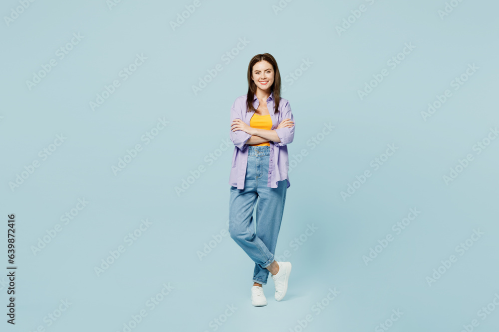 Full body young happy woman she wears purple shirt yellow t-shirt casual clothes look camera hold ahnds crossed folded isolated on plain pastel light blue background studio portrait Lifestyle concept