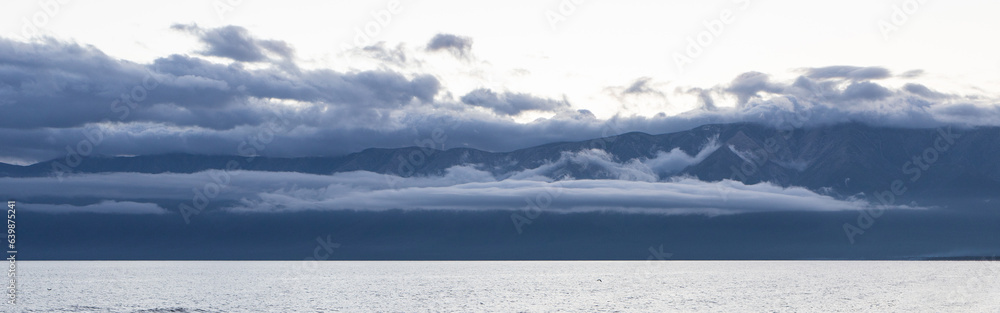 The water surface of Lake Baikal and the mountains on the horizon in the clouds. Chivyrkuysky Bay of Lake Baikal. Panoramic shooting,banner for your advertising