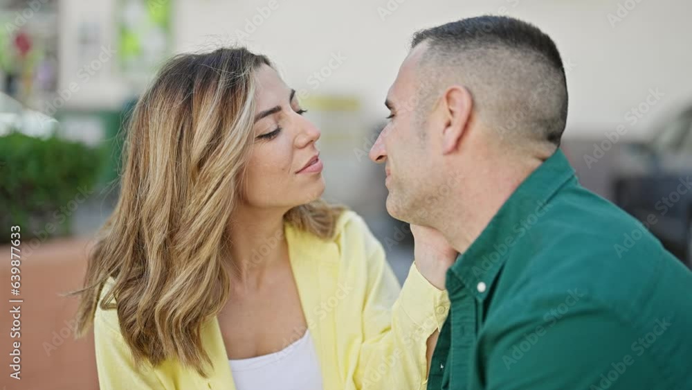 Man and woman couple sitting on bench together kissing at street Man and woman couple sitting on bench together kissing at street