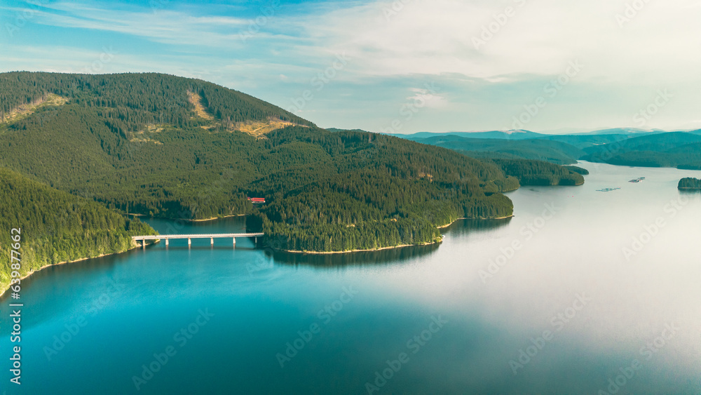 Spectacular landscape from a height. Lake, fir forest and a white bridge over the water.