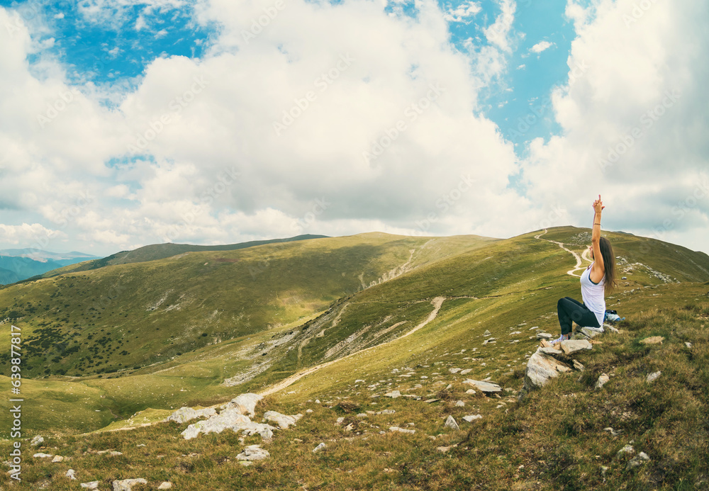 A young woman relaxes practicing Yoga exercises in a mountain landscape.